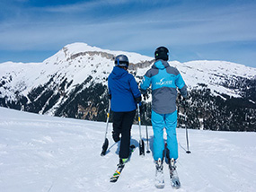 Zwei Skifahrer blicken ins Tal, einem Skifahrer fehlt ein Bein