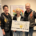 Stephanie Loick, Anette Blomberg, Christoph Loick bei der Spendenübergabe vor einem Bild, das Patient:innen gemalt haben